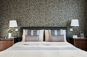 Geometrische Tapete mit Nachttischchen aus Holz im Schlafzimmer eines Londoner Hauses UK