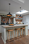 Black pendant lights above breakfast bar with wooden stools in 1930s Arts and Crafts home West Sussex UK