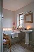 Quadratischer Spiegel über einem Sockelbecken mit einer Badewanne mit Nut und Feder am Fenster in einem Haus im Arts-and-Crafts-Stil in West Sussex, Großbritannien