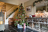 Lit candles on sideboard with Christmas tree in tiled hallway of detached Hampshire home
