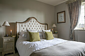 Double bed with buttoned headboard and lit candles in Hampshire home