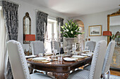 Silver candlesticks and lilies on vintage dining table with upholstered chairs in Wiltshire home England UK