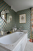 Gold and turquoise wallpaper with vintage mirror with marble bath surround in Wiltshire home England UK