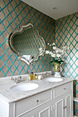 Goldgemusterte Tapete mit Vintage-Spiegel über Doppelwaschbecken in einem Haus in Wiltshire, England UK
