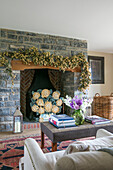 Flower garland above stone fireplace with ottoman in living room of Somerset farmhouse UK