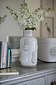 Cut flowers in ceramic vase with books on chest of drawers in Somerset farmhouse UK
