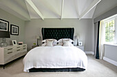 Dark green buttoned headboard with white covers on bed in Surrey home UK