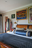 Framed artwork above double bed with blue bolster and oval mirror in West Sussex home UK