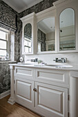 Double basins with mirrored cabinets and grey wallpaper and blinds in West Sussex home UK