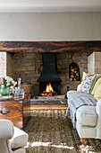 Sofa und Holztruhe am beleuchteten Kamin in einem Haus in Somerset, UK
