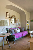 Hellrosa Decke auf tealfarbenem Sofa mit goldenem Spiegel in einem Haus in Somerset, UK