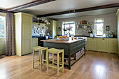 Yellow bar stools at green kitchen island in spacious Somerset home UK