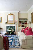 Rosa Kissen auf Sofa mit blau gemustertem Teppich im Wohnzimmer in Hampshire, UK