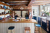 Ceramics on shelving with stools at bar in kitchen of 17th century Northamptonshire cottage UK