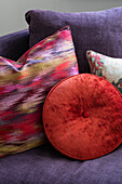 Red and patterned cushions on purple sofa in North London home UK