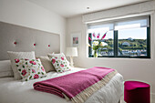 Pink blanket folded on double bed with floral cushions and view of Cornwall UK
