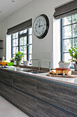 Clock above sink in modernised kitchen of 1900s Arts and Crafts style London home UK