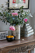 Rosa Rosen in einer Vase mit Büchern auf einem geschnitzten Holztisch in einem Haus in Oxfordshire, England