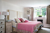 Pinker Bezug und großes Kopfteil auf einem Bett am Fenster in einem Haus in Oxfordshire, Vereinigtes Königreich