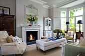 Lit fire with armchair and ottoman in London living room UK