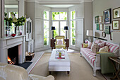 White ottoman with striped sofa and pair of black lamps in bay window in London living room UK