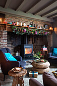 Grey armchairs at fireside with Christmas garland in Norfolk cottage England UK