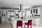 Red velvet barstools at kitchen island with stainless steel extractor in Hampshire home UK