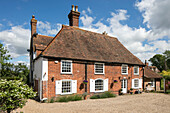 Gravel driveway and brick facade of Kent cottage with white painted shutters UK