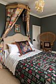 Gemischte Textilien auf einem Himmelbett mit Korbstuhl in einem dunkelgrauen Schlafzimmer in einem Landhaus in Kent UK
