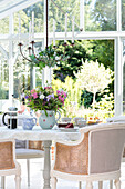 Korbstühle am Tisch mit Schnittblumen und Kaffeetasse im Wintergarten in Sussex UK