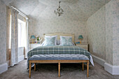 Karierte Decke auf einem Doppelbett mit geblümten Vorhängen und Tapeten in einem Haus in Sussex, UK