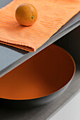 Orange on teatowel with bowl on grey shelving in London kitchen UK