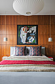 Modern art above double bed with cushions and wood panelling in London home UK