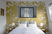 Artwork recessed to wall with gold floral paper above double bed in London home UK