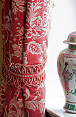 Rote geblümte Vorhänge mit Raffhalter und chinesischer Urne in einem Haus in Sussex