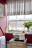 Glass bottles and wash stand with net curtains in window of Sussex bathroom