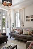 Gestreiftes braunes Sofa und Kissen mit weißen Vorhängen vor französischen Türen in einem Stadthaus in Issigeac im Perigord Frankreich