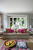 Striped cushions on beige sofa with apples on ottoman in Hampshire living room England UK