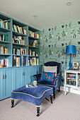 Blue velvet armchair and footstool with turquoise bookshelf in Hampshire home England UK
