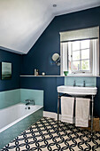 Monochrome tiles in teal bathroom with open window above sing Hampshire England UK