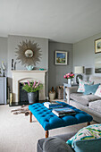 Sunburst mirror above fireplace with buttoned ottoman in Hampshire living room England UK