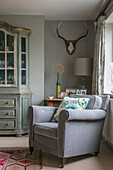 Light grey armchair and vintage cabinet in corner of Hampshire home England UK