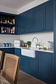 Belfast sink with bottles on shelving and blue paintwork in kitchen of North London apartment UK