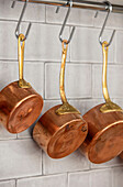 Three copper pans hanging on hooks in 1840s Cotswolds cottage Oxfordshire UK