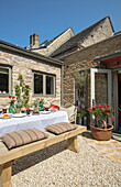 Table with cushions on bench seat in courtyard of 1840s Cotswolds cottage Oxfordshire UK
