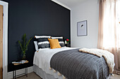 Wall painted Off Black with dyed cushions sheepskin and blanket on bed in Cumbrian terrace UK