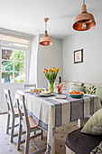 Tulips on striped tablecloth with copper pendants and cushions in Wiltshire cottage UK