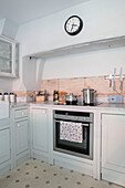 Clock above oven with pans on hob and walls in Pavilion Grey in Wiltshire kitchen UK