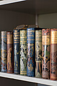 Gebundene Bücher bringen Farbe und Muster in ein Regal in einem Bauernhaus in Norfolk, Großbritannien