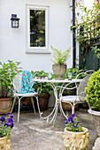 White metal table and chairs with container plants in courtyard of Surrey cottage UK